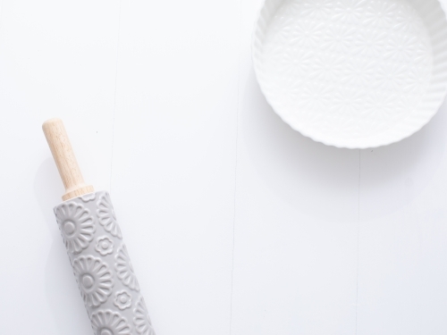 Ceramic pie dish and rolling pin on blank background