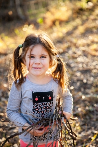 Cheeky little girl collecting sticks for kindling for a winter fire - Australian Stock Image