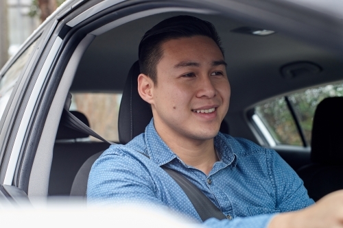 Cheerful Asian man driving in car