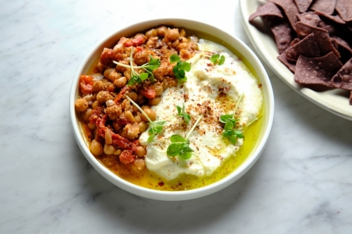 Chickpeas and tomato sofrito in a white bowl with chocolate taco chips on the side - Australian Stock Image