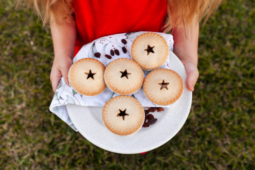 Child carrying plate of fruit mince pies to share outside in backyard at Christmas   - Australian Stock Image