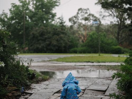 Child in blue raincoat walking out into the rain