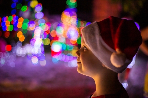 child in santa hat looking at a Christmas light display