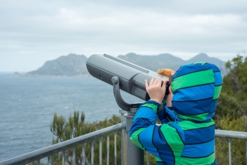 Child looking through binoculars at cliffs and ocean