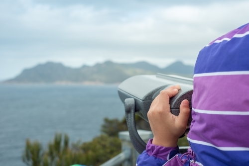 Child looking through binoculars at cliffs and ocean - Australian Stock Image