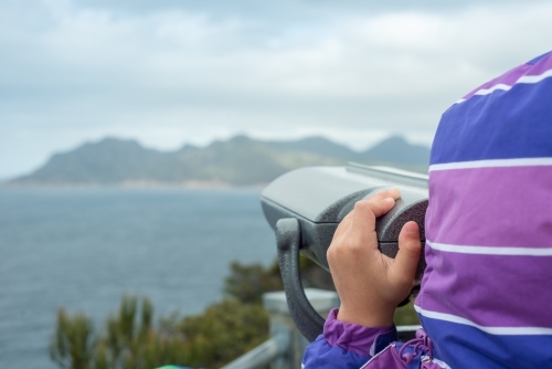Child looking through binoculars at cliffs and ocean