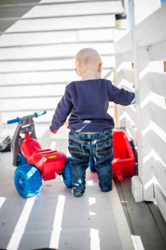 Child on white verandah with toy bike and trailer - Australian Stock Image