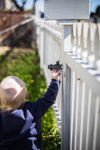 Child reaching up to open gate on white fence