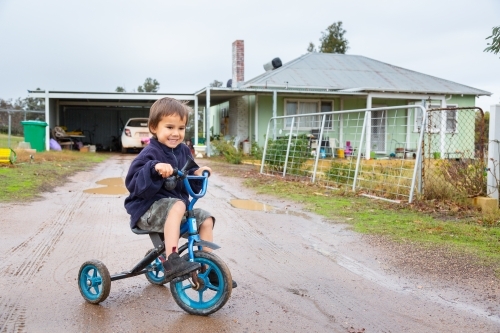Child riding tricycle in puddles - Australian Stock Image