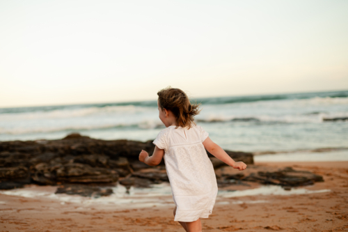 Child running along the beach at sunset, enjoying the waves and sandy shore - Australian Stock Image