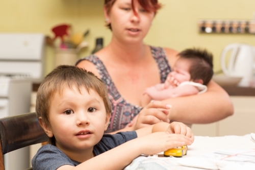 Child sitting at table with mother and baby behind - Australian Stock Image