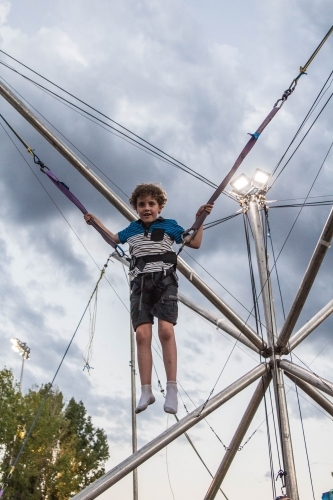 Child strapped into harness on ride at show jumping in air smiling - Australian Stock Image