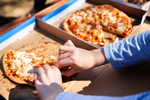 Child taking slice of takeaway pizza from box - Australian Stock Image