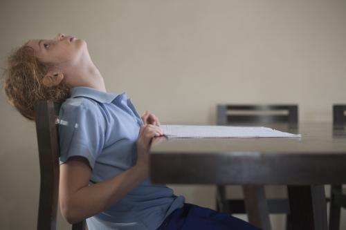 Child tired of doing school homework at wooden desk.