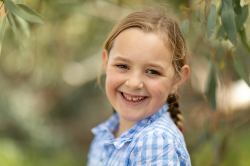 child with baby teeth smiling at camera with blurry leafy background