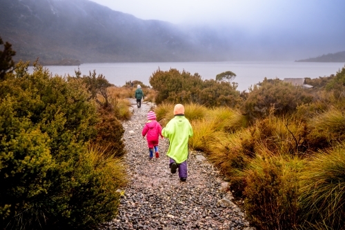 Children in bright rain jackets running down path on overcast day - Australian Stock Image