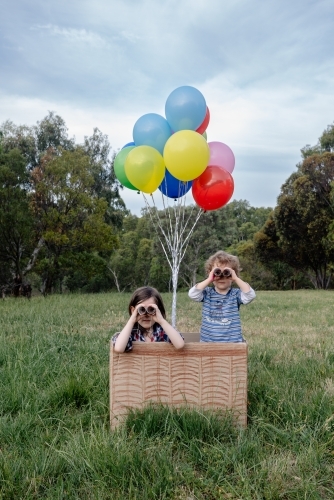 Children play in hot air balloon made from a box & balloons, looking through toilet roll binoculars - Australian Stock Image