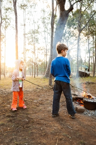 Children poking sticks into campfire at campsite - Australian Stock Image