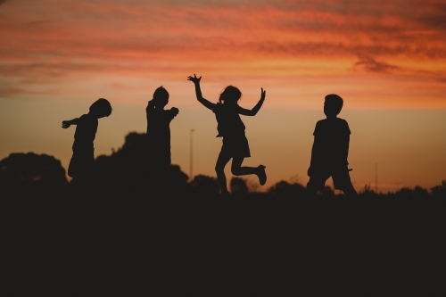 Children silhouette playing at sunset with girl jumping