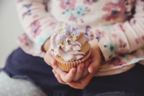 Childs hands holding purple flower cupcake - Australian Stock Image
