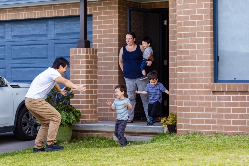 Chinese Australian dad arriving home from work greeting family - Australian Stock Image