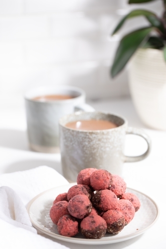 Chocolate protein balls on a white kitchen bench with two mugs