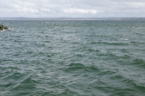 Choppy waves with land along the horizon and clouds in sky - Australian Stock Image