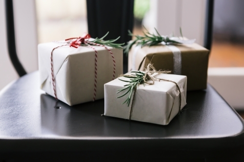 Christmas gifts in neutral wrapping sitting on a dining chair - Australian Stock Image