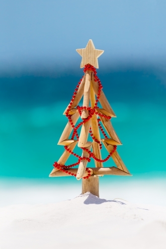 Christmas tree on idyllic white sandy beach with ocean background blur - Australian Stock Image