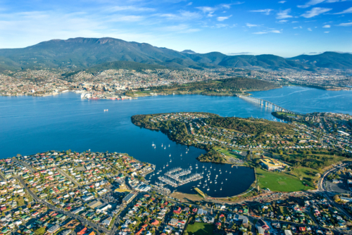 City sprawling around a wide blue harbour beneath green mountains. - Australian Stock Image