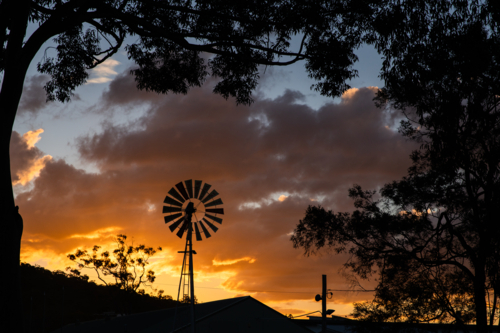 Classic windmill stands tall in silhouette at sunset - Australian Stock Image