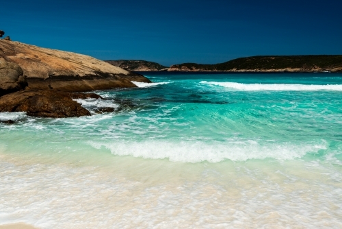 Clear turquoise ocean water washing up on sand with rocky point.