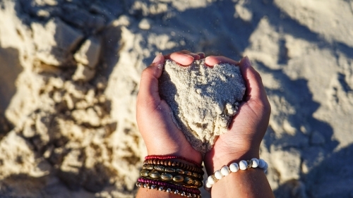 Close of hands holding sand in heart shape