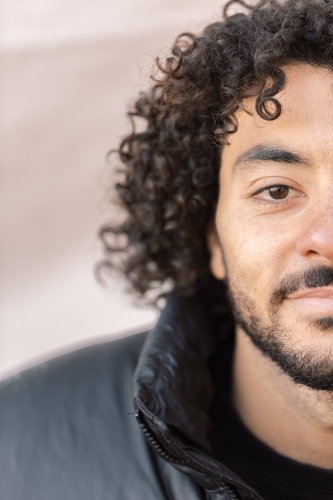Close up and half face shot of a smiling young man with a curly hair and beard - Australian Stock Image