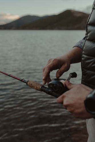 Close up detail shot of hands adjusting a reel while fishing - Australian Stock Image