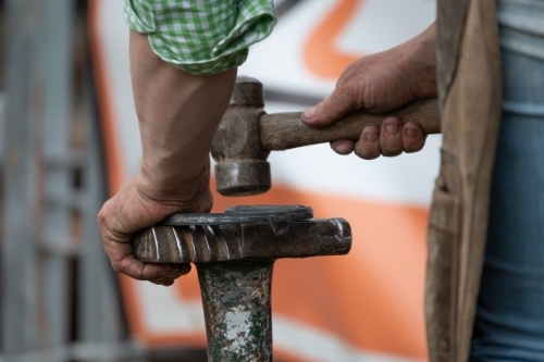 Close up of a farrier shaping a horse shoe with a hammer - Australian Stock Image