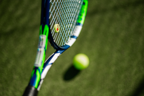 Close-up of a tennis racquet poised near a bright green tennis ball on grass - Australian Stock Image