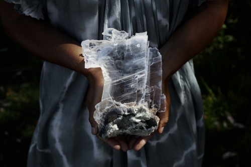 Close up of a woman holding a dark, selenite crystal on geode