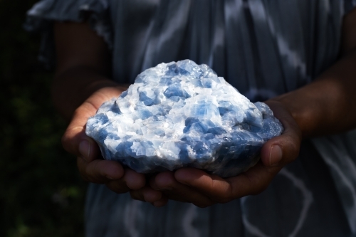 Close up of a woman holding a healing blue calcite crystal in her hands in moody lighting
