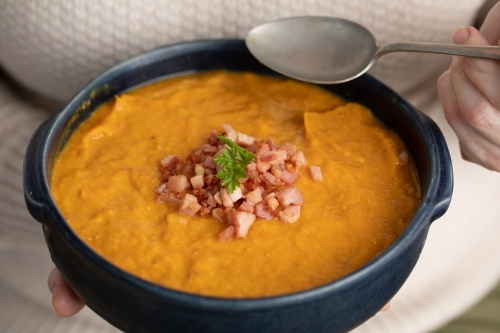 close up of blue bowl of pumpkin soup in lady hands and spoon