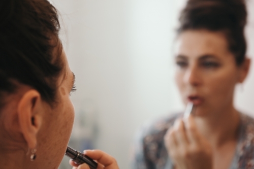 Close up of brunette woman applying makeup with blurred mirror reflection - Australian Stock Image