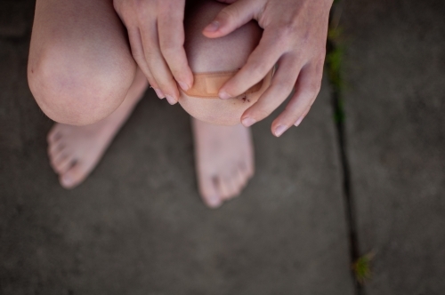 Close up of child's hands putting plaster on grazed knee