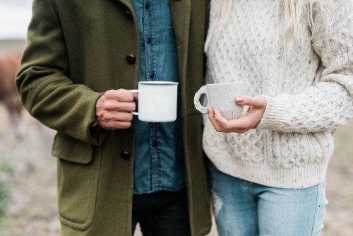 Close up of couple holding cups of coffee outside on farm - Australian Stock Image