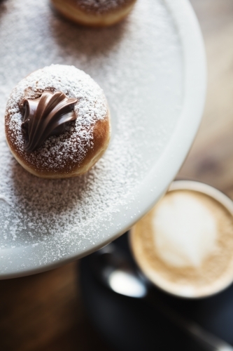 Close up of delicious chocolate topped donuts on a marble platter with coffee below - Australian Stock Image