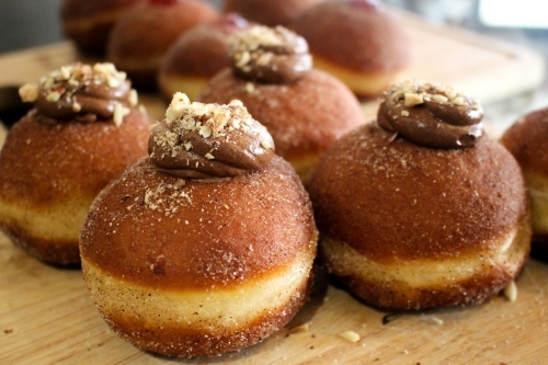 Close up of freshly baked doughnuts filled with chocolate ganache and sprinkled with hazelnuts - Australian Stock Image