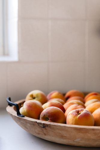 Close up of freshly picked ripe peaches in a wooden bowl on white kitchen bench - Australian Stock Image