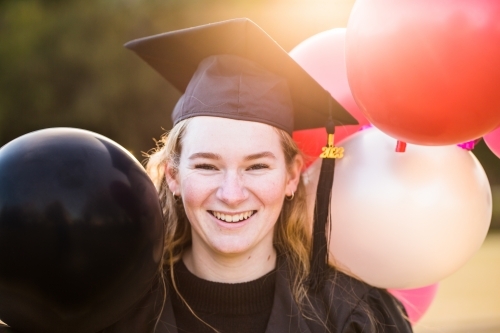 Close up of girl smiling in graduation cap with balloons - Australian Stock Image