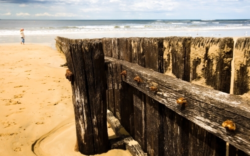 Close up of groyne with young girl walking in background - Australian Stock Image