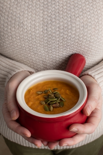 close up of hands holding bowl of pumpkin soup - Australian Stock Image