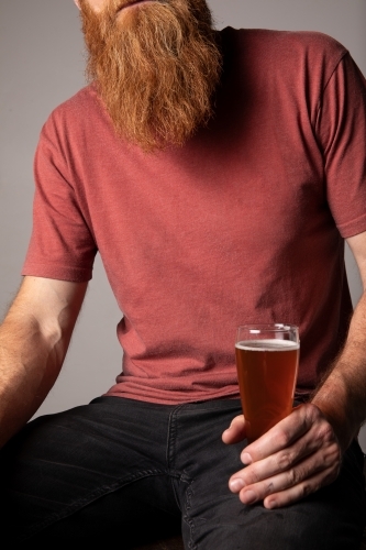 Close-up of man's ginger beard, him holding a glass of beer - Australian Stock Image